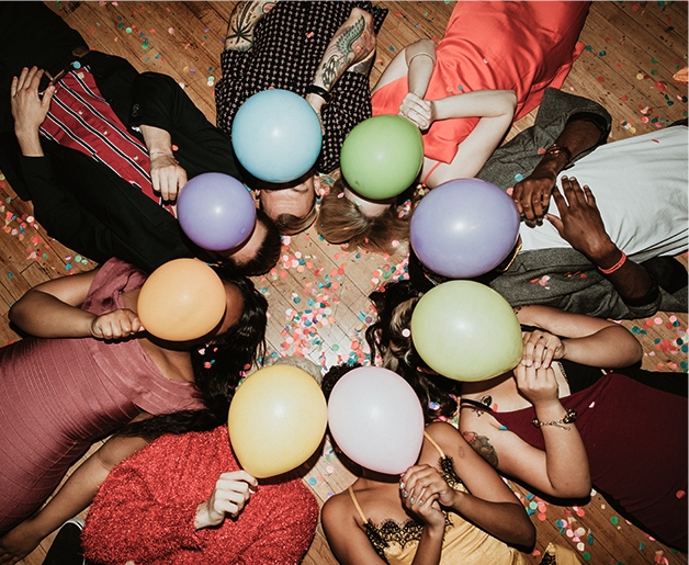 friends lying down together holding colorful balloons