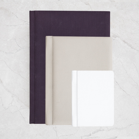 Three-photo-books-in-different-sizes-in-portrait-orientation-and-colors-displayed-on-a-light-marble-background-featuring-a-sleek-and-minimalist-design