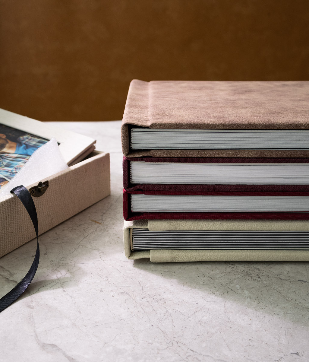 luxury hardcover photo albums stacked on a marble surface featuring suede and leather covers in beige brown and burgundy elegant wedding photo book collection